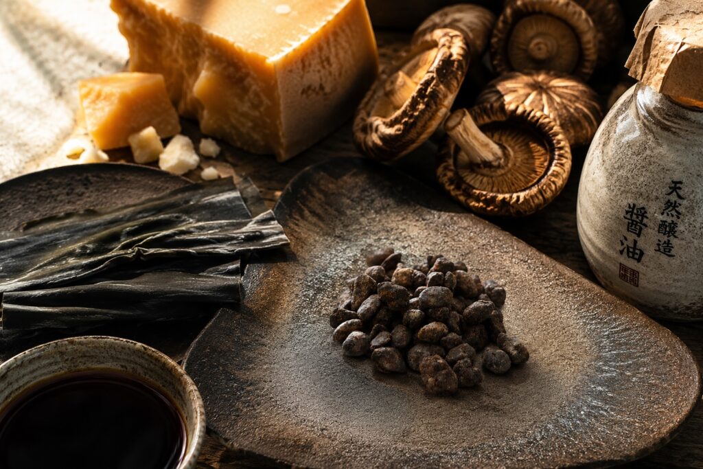 Authentic Hamanatto displayed beside naturally glutamate-rich ingredients including kombu, Parmesan, soy sauce, and shiitake mushrooms.